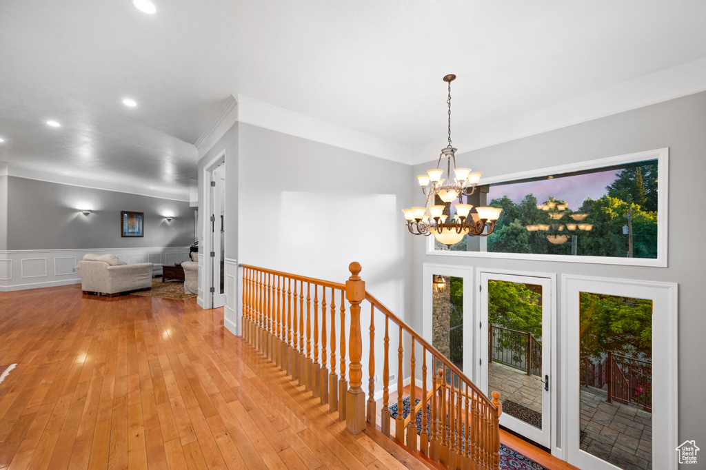Hall with a notable chandelier, ornamental molding, and light hardwood / wood-style floors