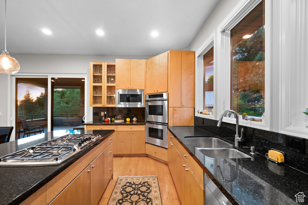 Kitchen featuring dark stone counters, decorative light fixtures, light hardwood / wood-style floors, appliances with stainless steel finishes, and sink