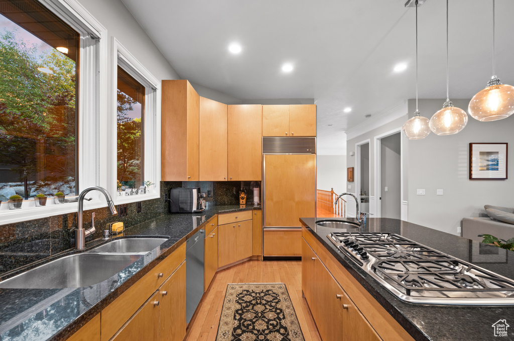 Kitchen with decorative light fixtures, backsplash, light hardwood / wood-style flooring, sink, and paneled built in fridge