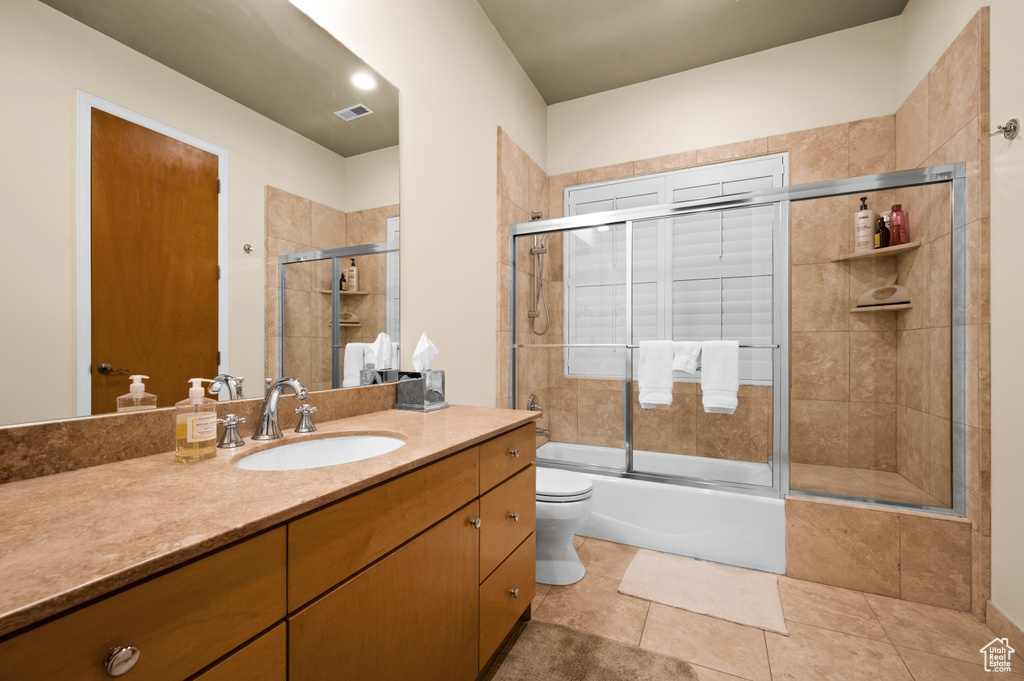 Full bathroom with combined bath / shower with glass door, vanity with extensive cabinet space, tile flooring, and toilet