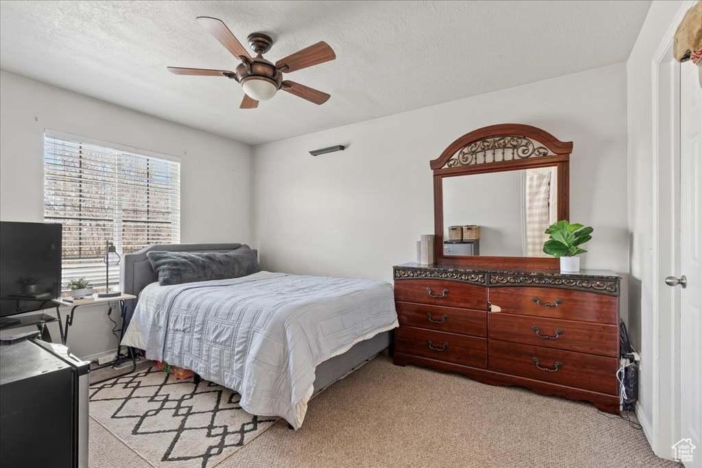 Bedroom with ceiling fan, light colored carpet, and a textured ceiling