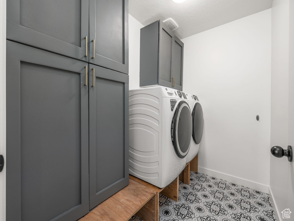 Washroom with cabinets, light tile floors, and washer and clothes dryer