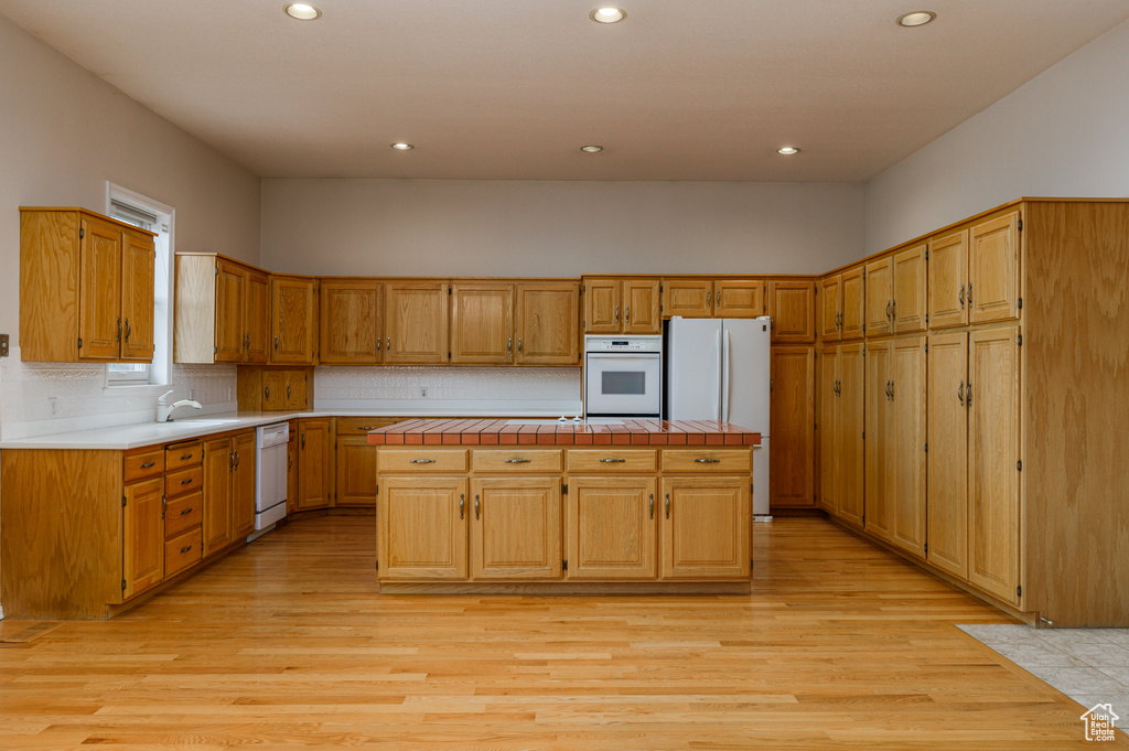 Kitchen with white appliances, light wood-type flooring, tasteful backsplash, and a center island