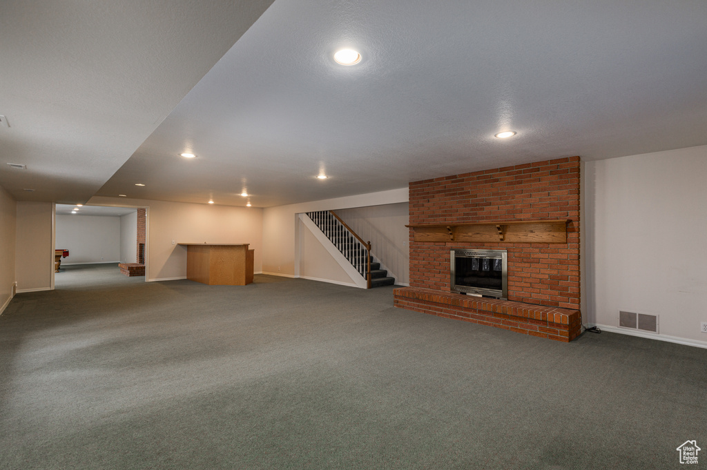 Unfurnished living room with brick wall, dark colored carpet, and a fireplace