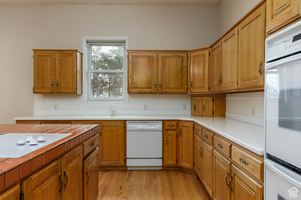 Kitchen with tasteful backsplash, white appliances, sink, and light wood-type flooring