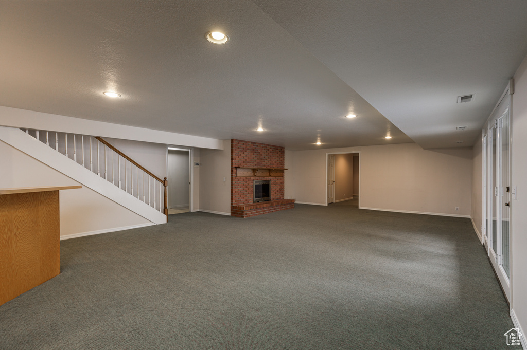 Basement featuring a brick fireplace, brick wall, and dark colored carpet