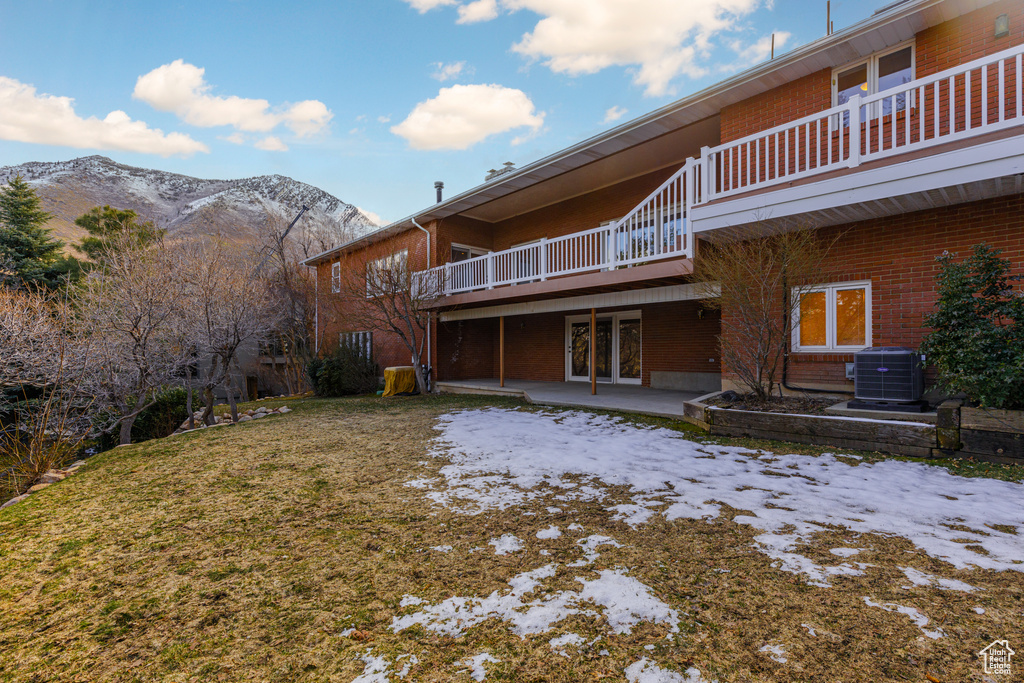 Back of property with a mountain view, a balcony, central air condition unit, a lawn, and a patio area