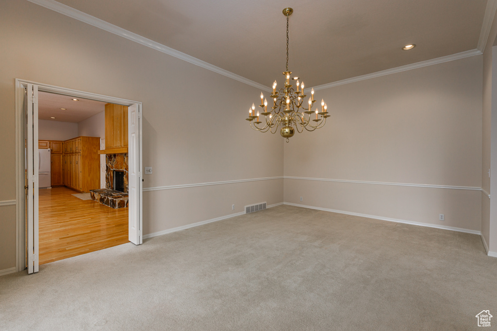 Carpeted empty room featuring ornamental molding, a stone fireplace, and an inviting chandelier