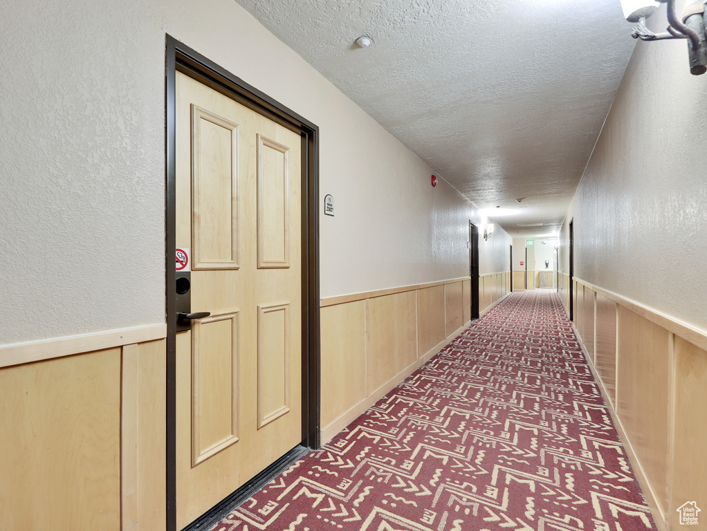 Hall featuring a textured ceiling and dark carpet