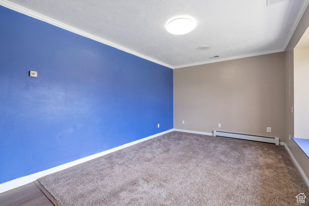 Spare room with baseboard heating, a textured ceiling, ornamental molding, and carpet flooring