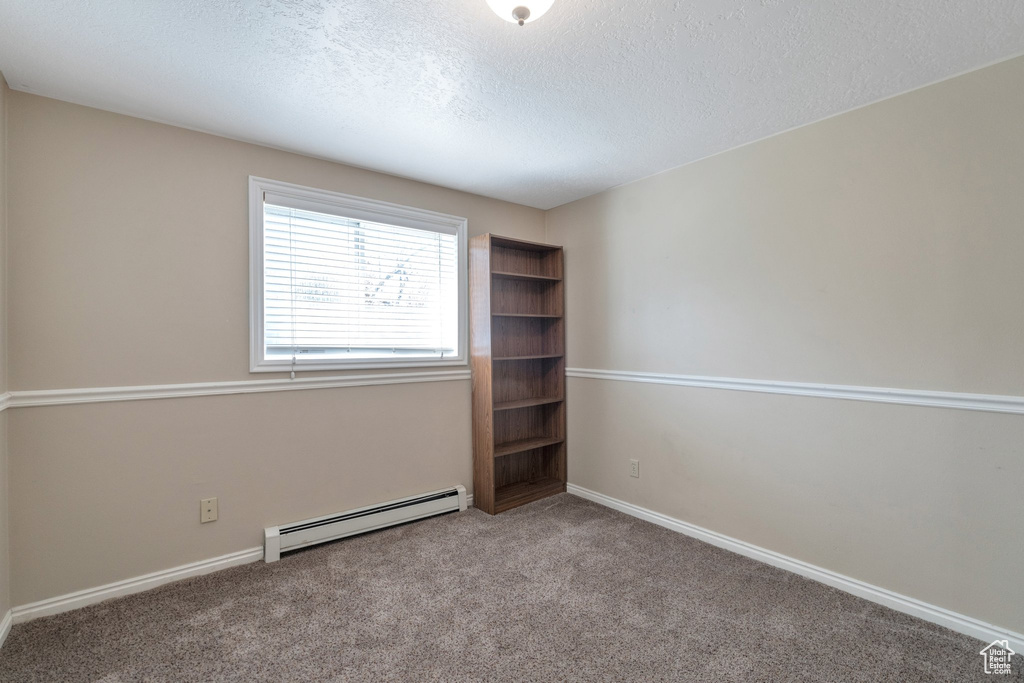Empty room featuring light carpet, baseboard heating, and a textured ceiling