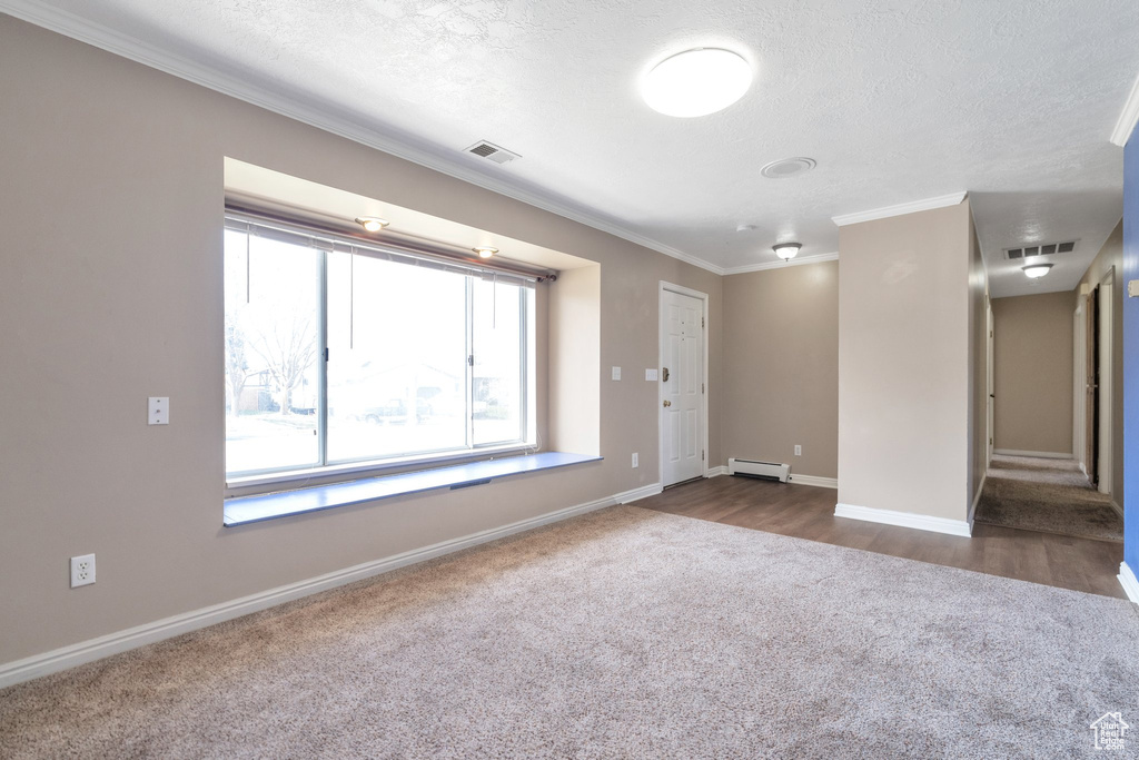 Empty room featuring dark carpet, ornamental molding, a textured ceiling, and baseboard heating