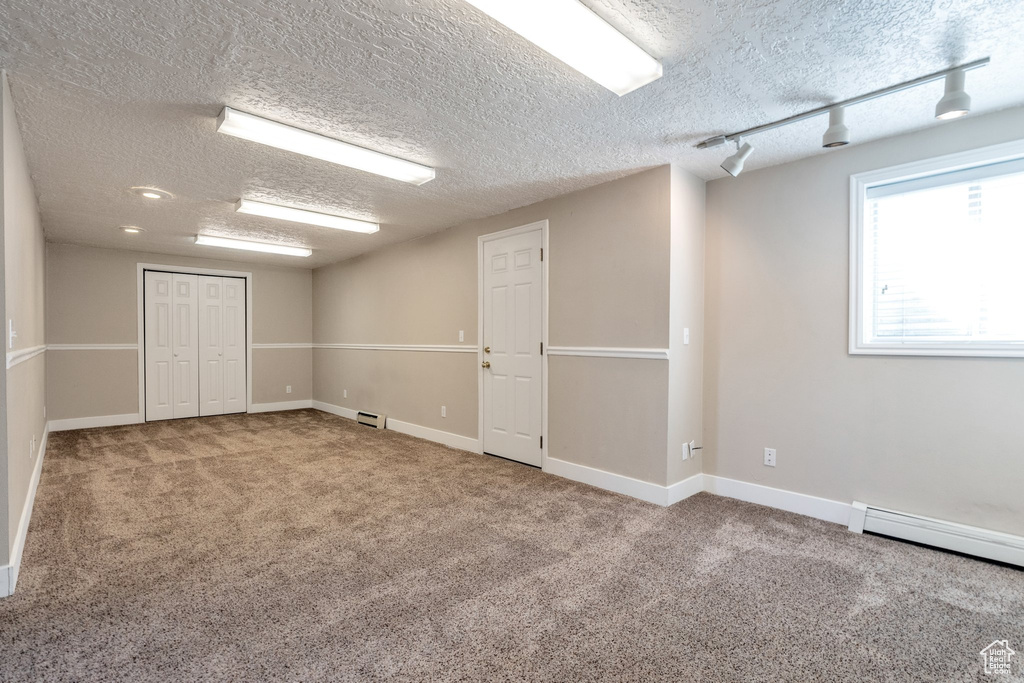 Carpeted spare room featuring a baseboard radiator and a textured ceiling