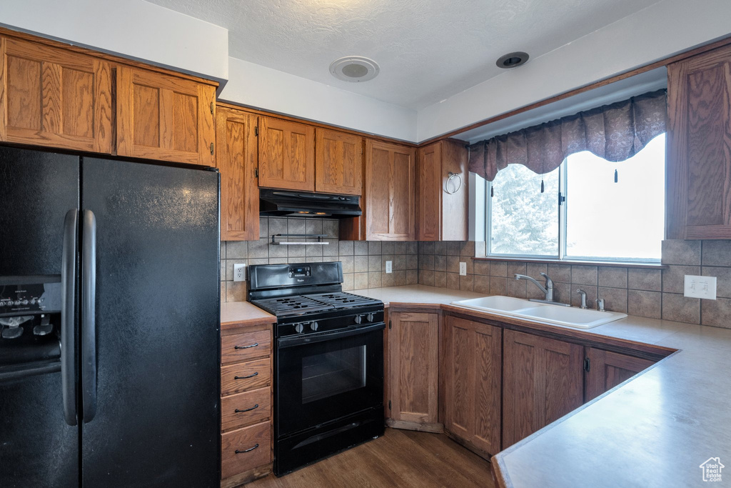 Kitchen featuring dark hardwood / wood-style floors, tasteful backsplash, sink, and black appliances