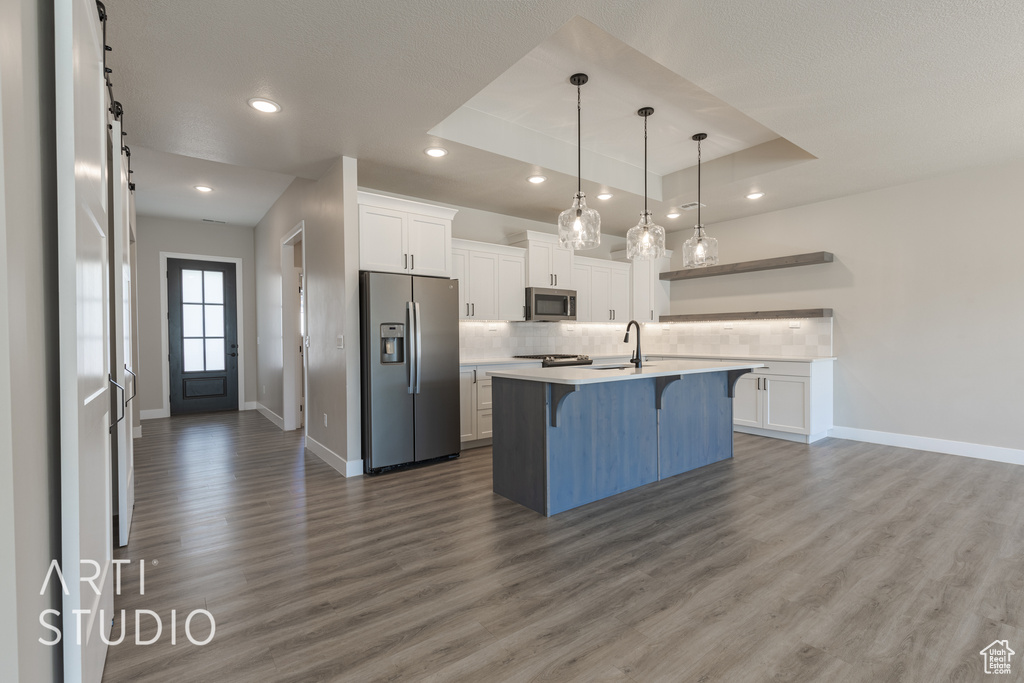 Kitchen featuring a kitchen island with sink, hardwood / wood-style floors, a tray ceiling, appliances with stainless steel finishes, and a breakfast bar area