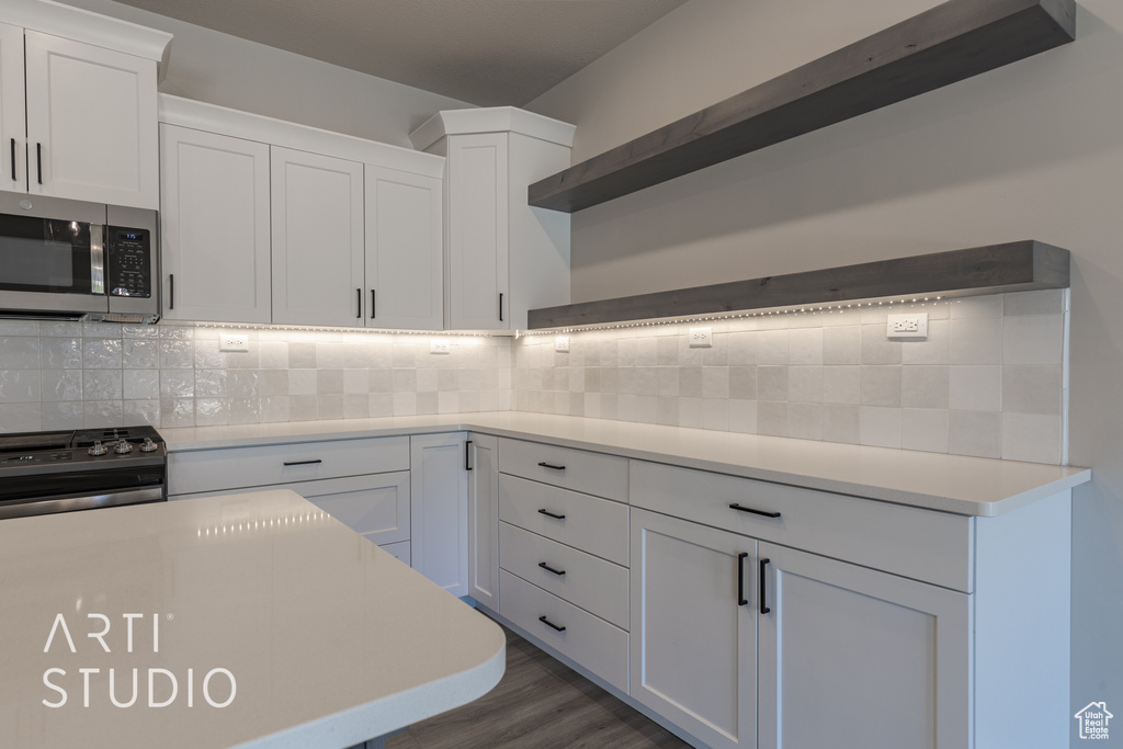 Kitchen with white cabinets, dark hardwood / wood-style floors, tasteful backsplash, and stainless steel appliances