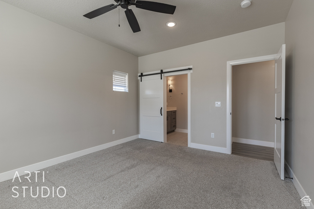 Unfurnished bedroom featuring carpet flooring, a barn door, connected bathroom, and ceiling fan