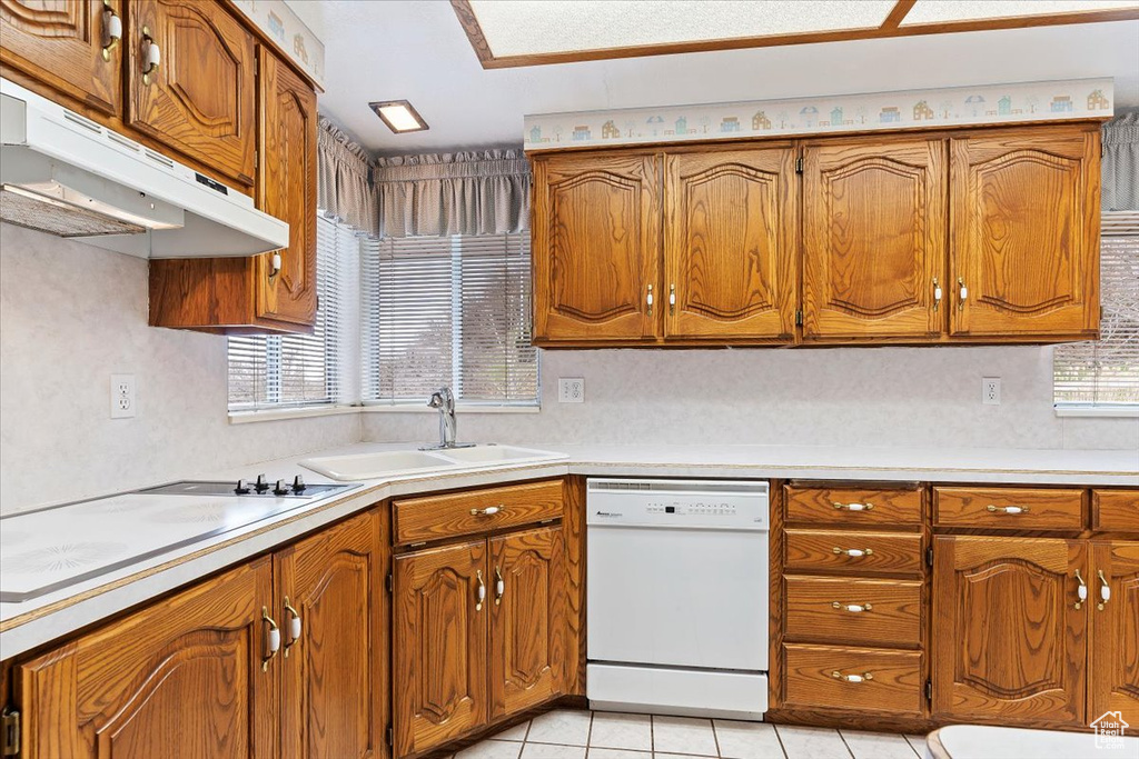 Kitchen featuring electric stovetop, sink, light tile flooring, and white dishwasher