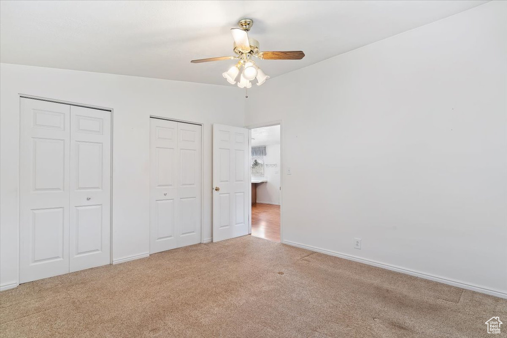 Unfurnished bedroom with light colored carpet, ceiling fan, lofted ceiling, and two closets
