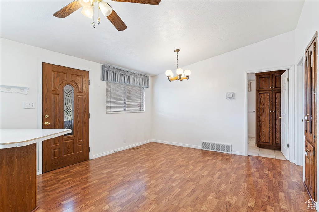 Empty room with light wood-type flooring and ceiling fan with notable chandelier