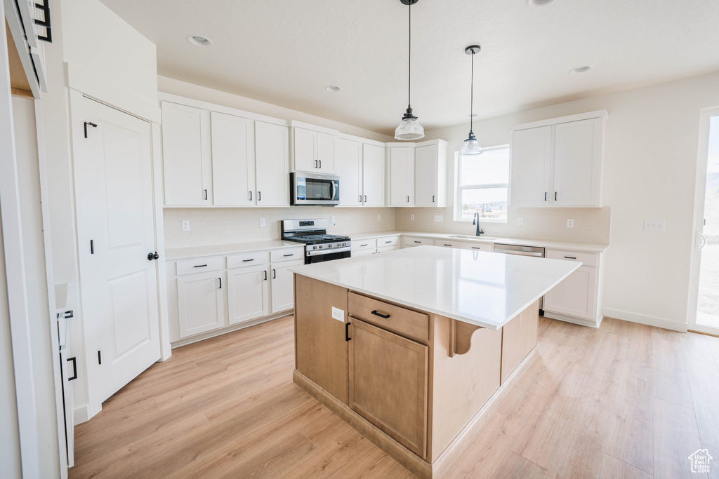 Kitchen with a kitchen island, light hardwood / wood-style flooring, stainless steel appliances, and white cabinetry