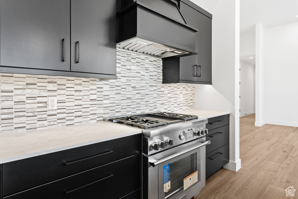 Kitchen featuring backsplash, high end stainless steel range, custom exhaust hood, and light wood-type flooring