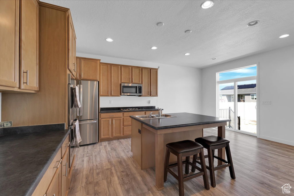 Kitchen with a breakfast bar area, a center island with sink, stainless steel appliances, and hardwood / wood-style flooring