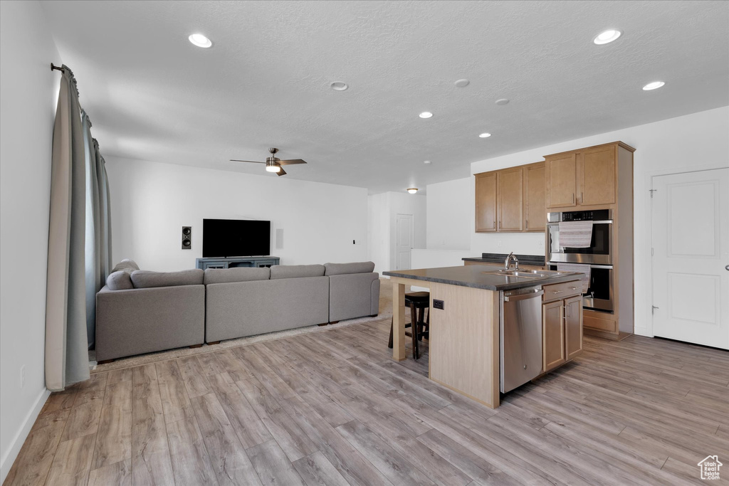 Kitchen featuring ceiling fan, a breakfast bar, appliances with stainless steel finishes, light hardwood / wood-style floors, and an island with sink