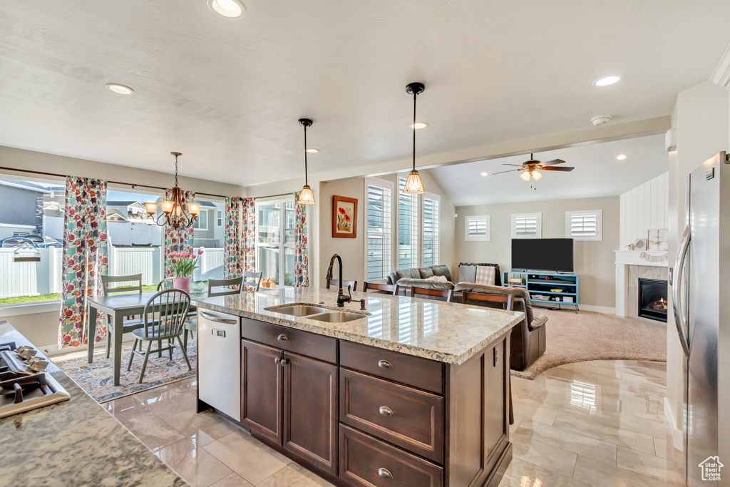 Kitchen featuring an island with sink, pendant lighting, light stone countertops, ceiling fan with notable chandelier, and sink