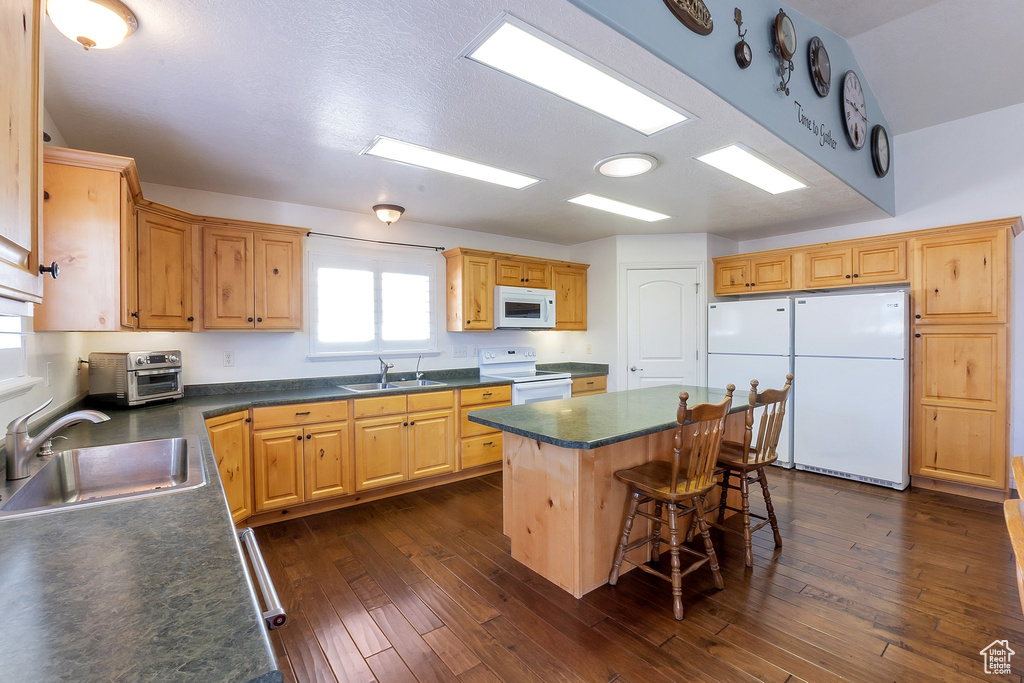 Kitchen featuring dark hardwood / wood-style flooring, a breakfast bar, a kitchen island, white appliances, and sink