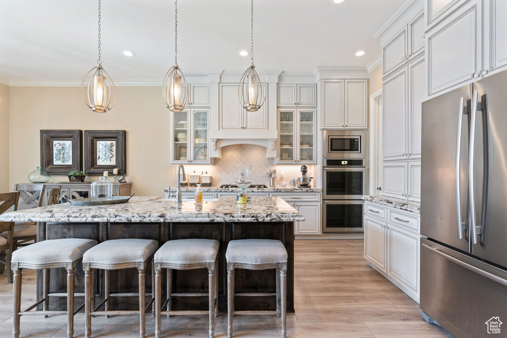 Kitchen with appliances with stainless steel finishes, a breakfast bar, an island with sink, light hardwood / wood-style floors, and tasteful backsplash