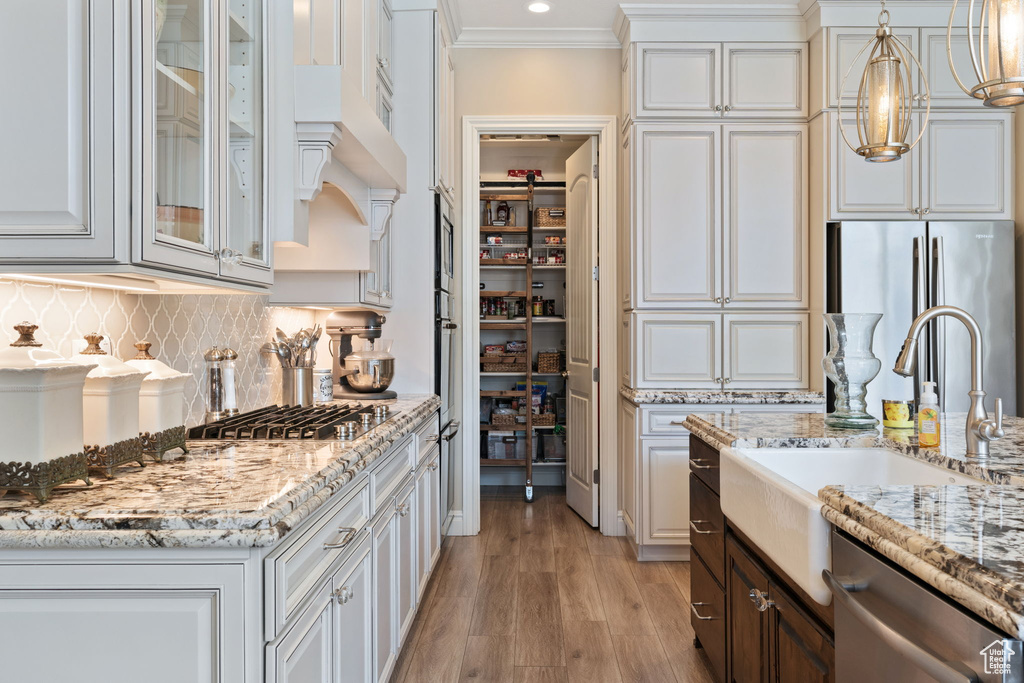 Kitchen featuring appliances with stainless steel finishes, tasteful backsplash, white cabinetry, crown molding, and light hardwood / wood-style flooring
