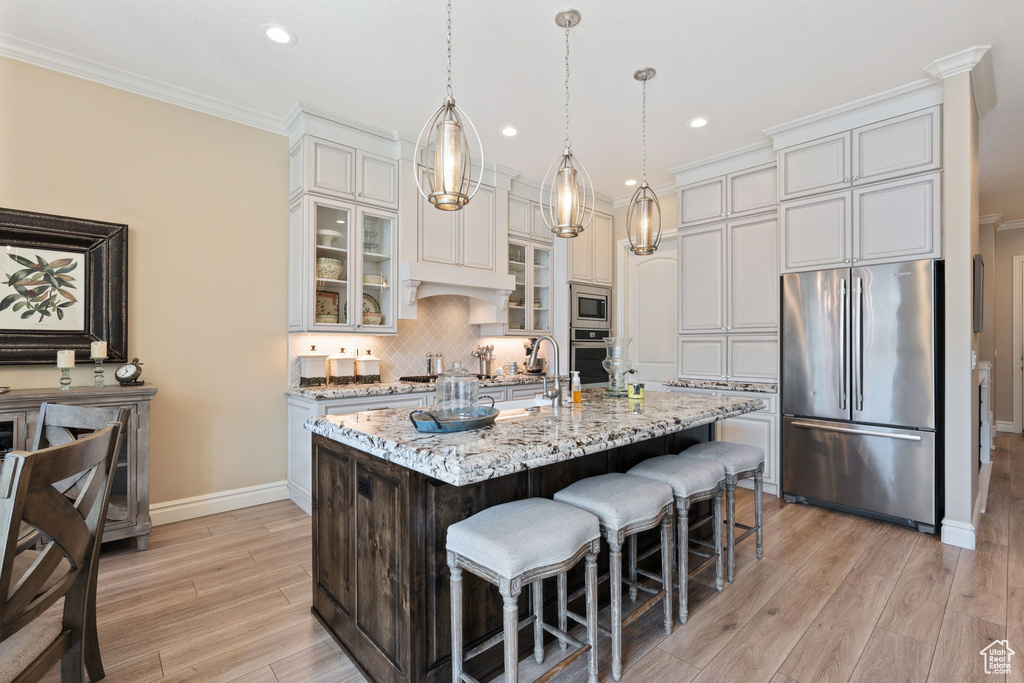 Kitchen with stainless steel appliances, backsplash, pendant lighting, light stone counters, and a center island with sink