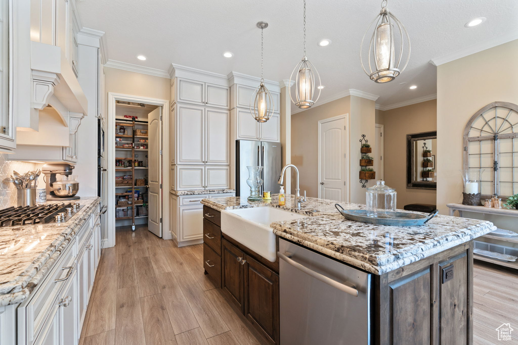 Kitchen featuring stainless steel appliances, light hardwood / wood-style floors, sink, a center island with sink, and white cabinets