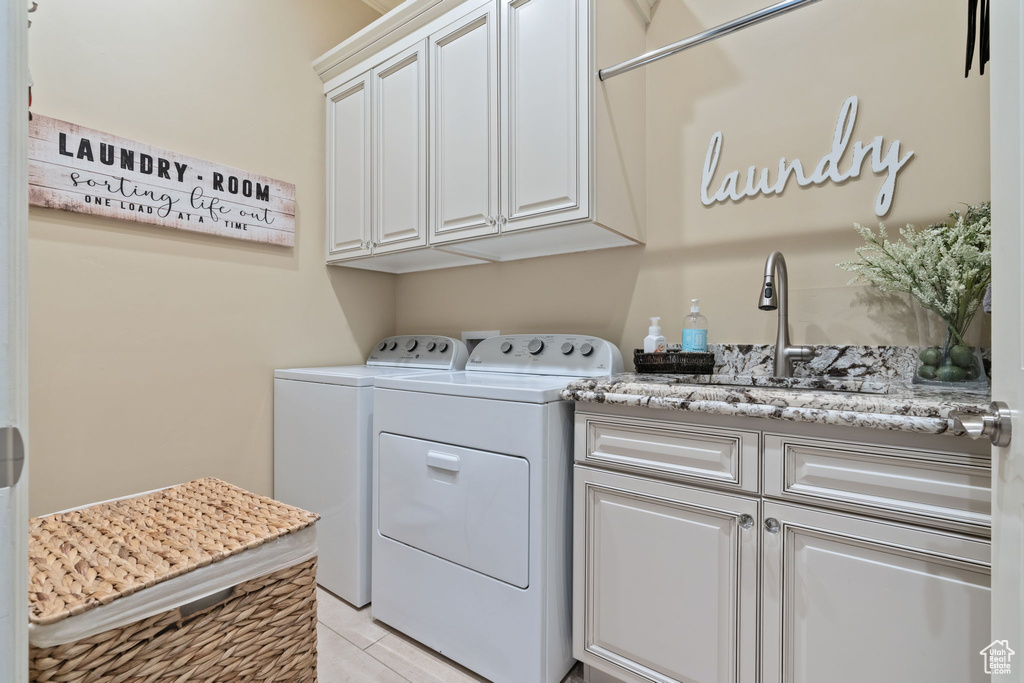 Clothes washing area with light tile floors, independent washer and dryer, cabinets, and sink