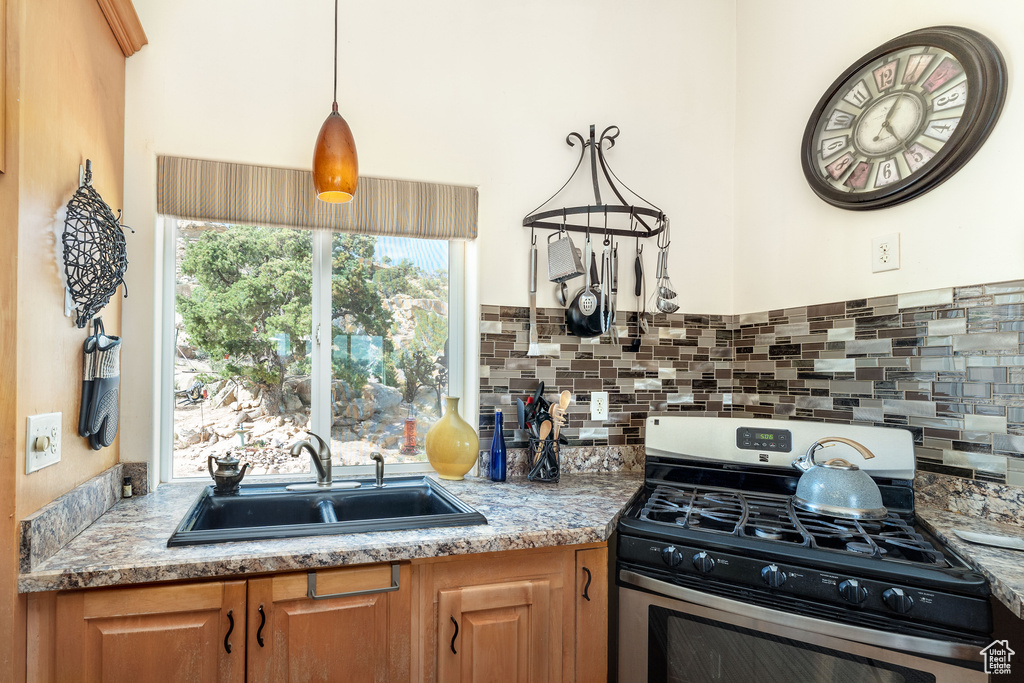Kitchen with backsplash, hanging light fixtures, gas range, and sink
