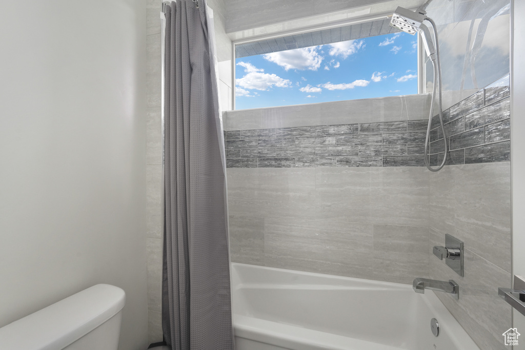 Bathroom featuring toilet and shower / bathtub combination with curtain