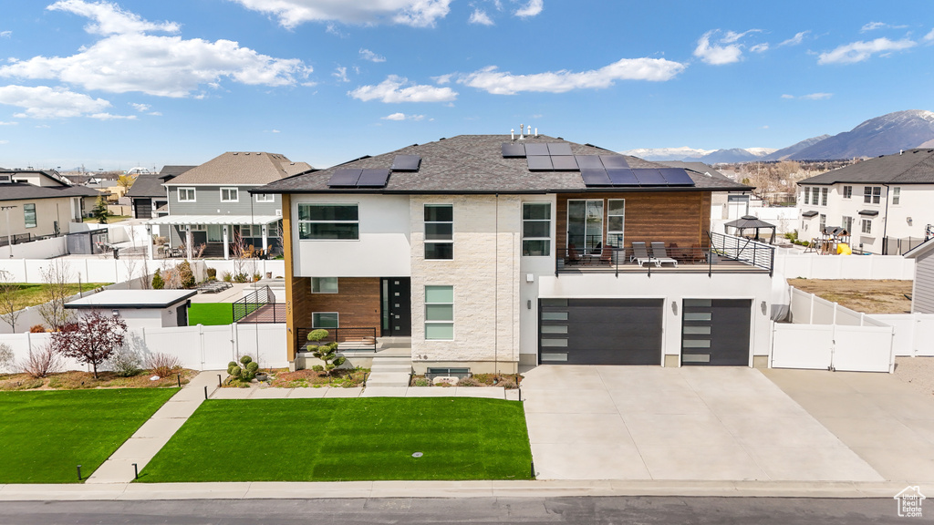 View of front of home with a balcony, a front yard, solar panels, a mountain view, and a garage