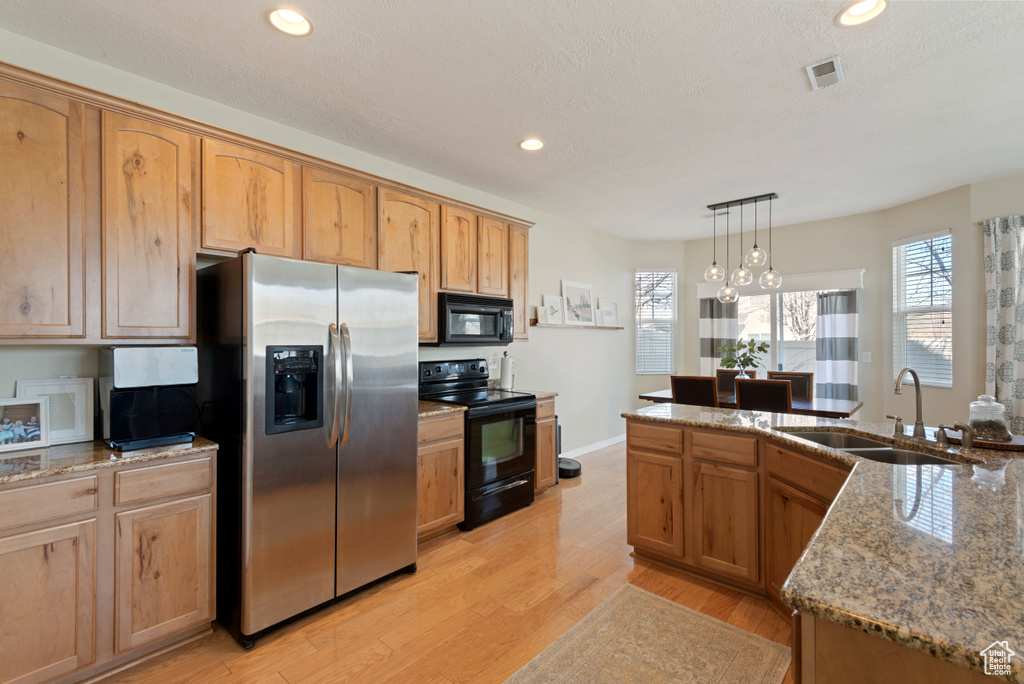 Kitchen featuring decorative light fixtures, sink, light hardwood / wood-style flooring, light stone countertops, and black appliances