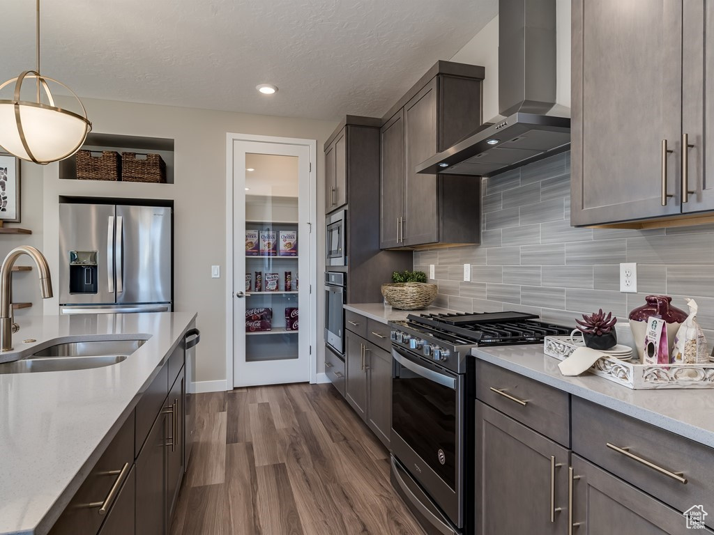 Kitchen featuring stainless steel appliances, backsplash, dark hardwood / wood-style floors, wall chimney exhaust hood, and hanging light fixtures