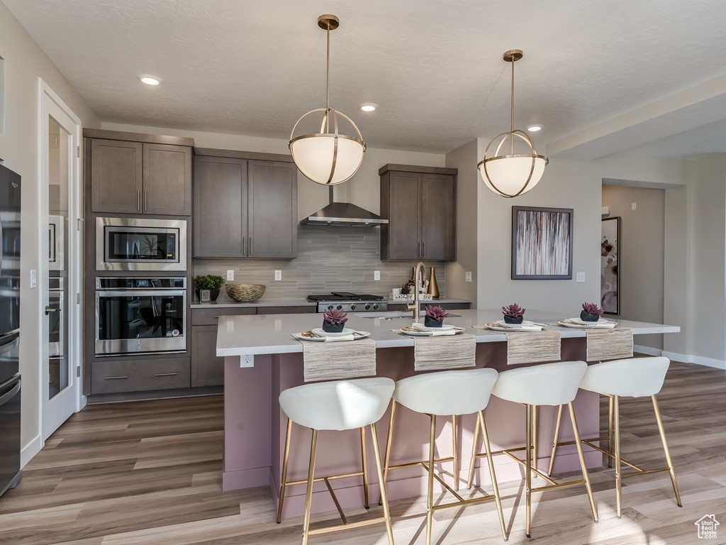 Kitchen with decorative light fixtures, backsplash, appliances with stainless steel finishes, and a kitchen island with sink