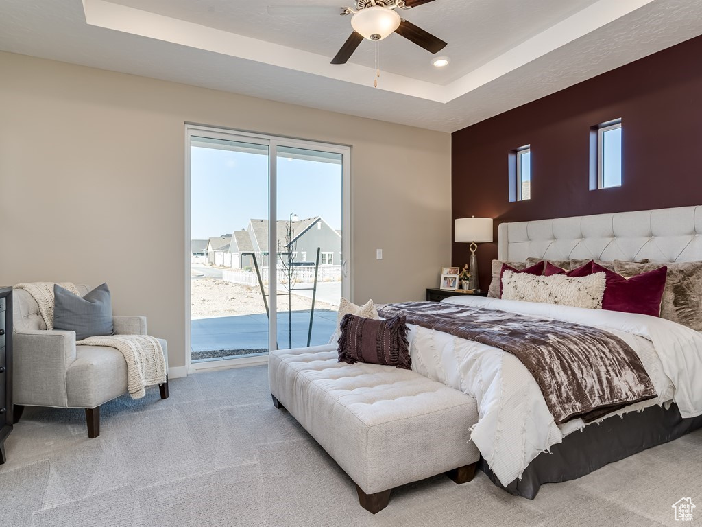 Carpeted bedroom with access to exterior, ceiling fan, a tray ceiling, and multiple windows