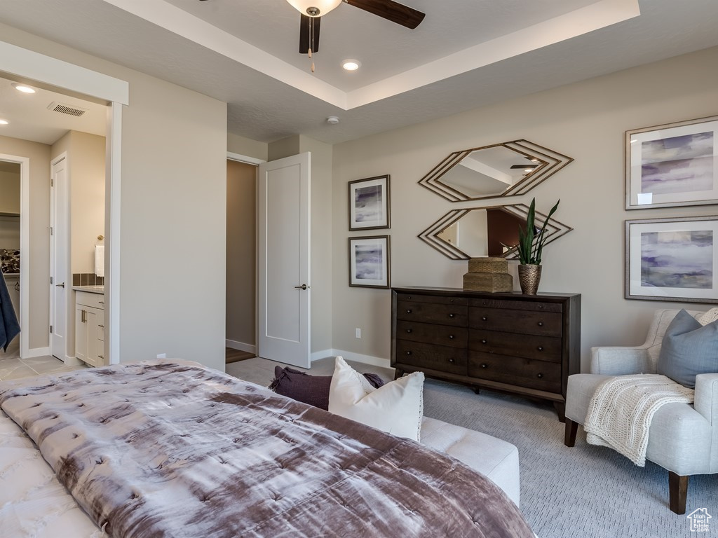 Bedroom with ceiling fan, a tray ceiling, light colored carpet, and ensuite bathroom