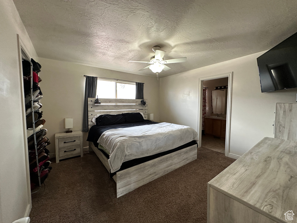 Bedroom with ensuite bath, a textured ceiling, ceiling fan, and dark colored carpet