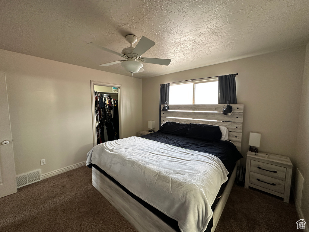 Carpeted bedroom featuring ceiling fan, a textured ceiling, a walk in closet, and a closet