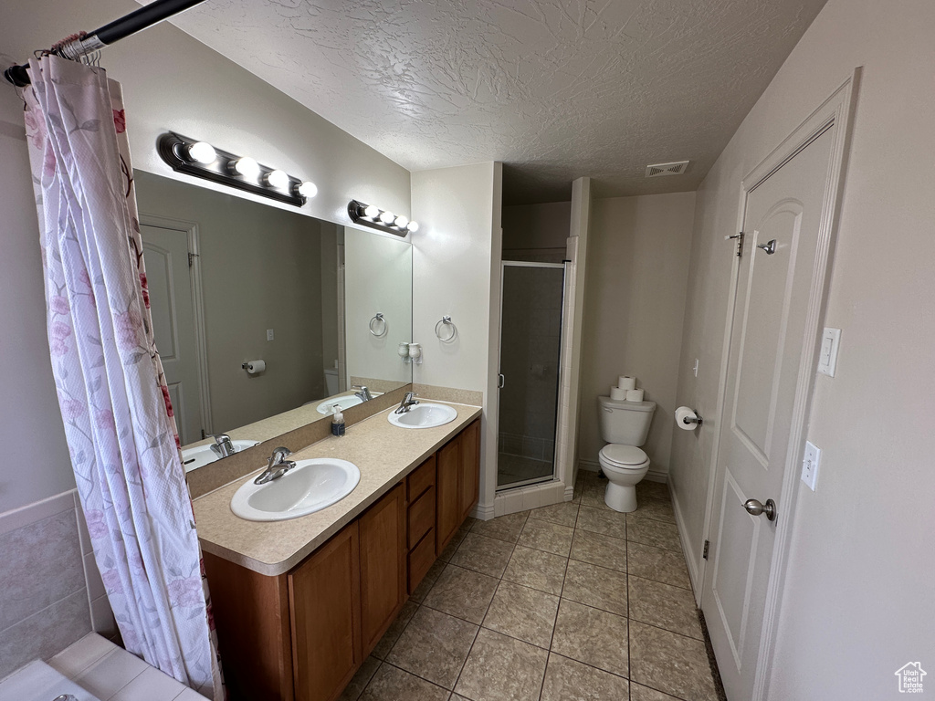 Bathroom with tile flooring, toilet, vanity with extensive cabinet space, double sink, and an enclosed shower