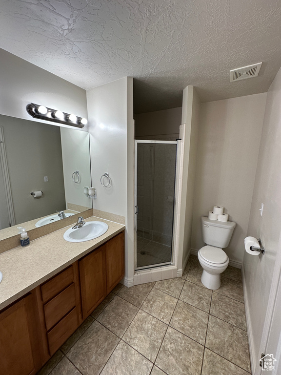 Bathroom featuring tile flooring, a shower with door, a textured ceiling, toilet, and vanity with extensive cabinet space