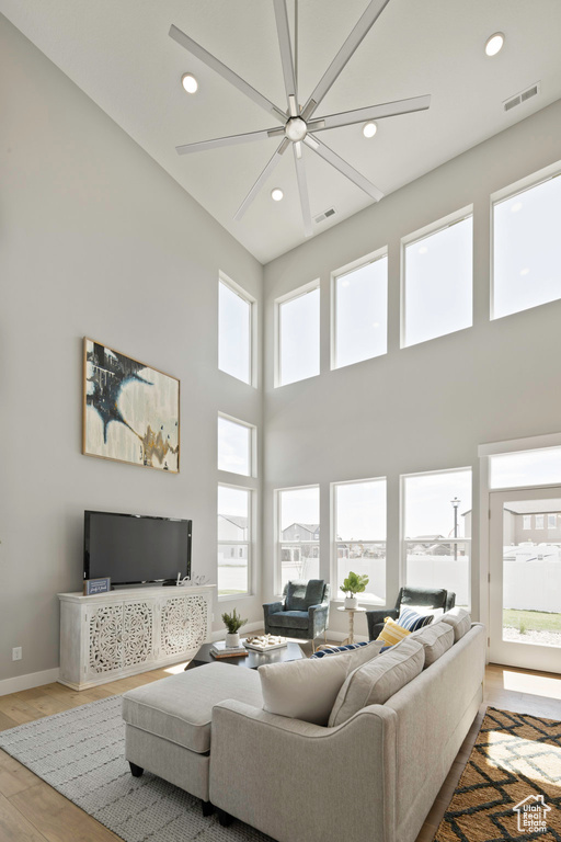 Living room featuring ceiling fan, a high ceiling, and light hardwood / wood-style floors