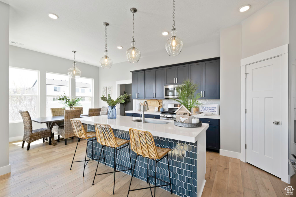 Kitchen featuring tasteful backsplash, stainless steel appliances, light wood-type flooring, and pendant lighting