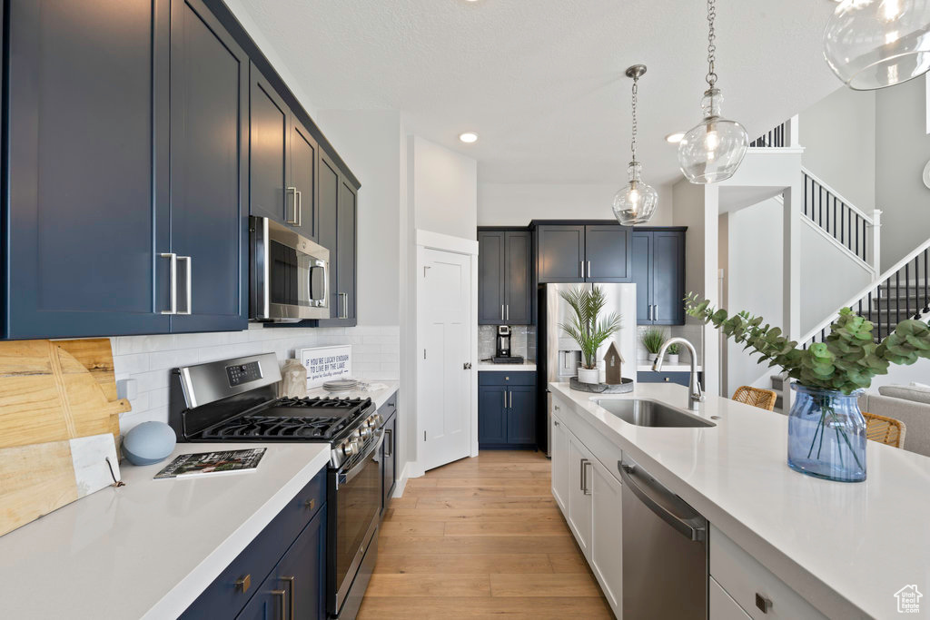 Kitchen with appliances with stainless steel finishes, tasteful backsplash, light hardwood / wood-style flooring, pendant lighting, and sink